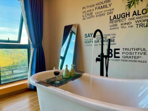 une baignoire avec un miroir et deux verres de vin dans l'établissement Pine Forest House Dalat, à Xuan An