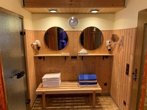 a bathroom with three mirrors and a bench with towels at Hotel Märchenwald in Haidmühle