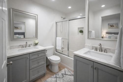 a white bathroom with two sinks and a toilet at The Olympic Suites LA in Los Angeles