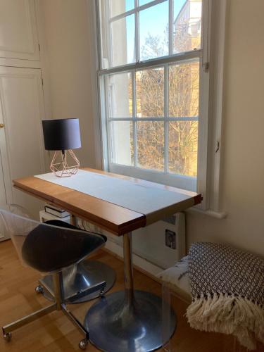 a desk with a lamp and a chair in front of a window at Luxurious tranquil large bedroom and bathroom suite with rooftop views in interior designed Georgian Townhouse in London