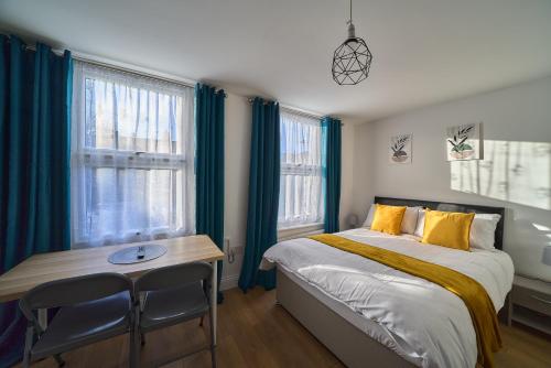 a bedroom with a bed and a desk and two windows at Chapel Road Cosy Rooms & Studios in Hounslow