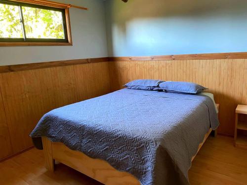 ein Schlafzimmer mit einem Bett mit blauen Laken und einem Fenster in der Unterkunft Cabaña equipada a 5 minutos de Panguipulli in Huellahue