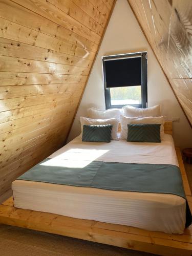 a bed in a wooden room with a window at Feeria Land Aframe in Radoşi
