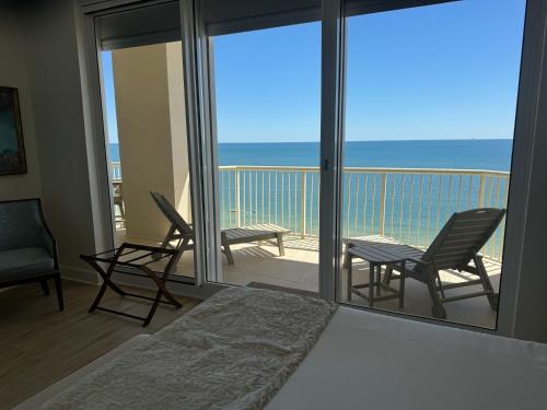 een slaapkamer met een bed en stoelen op een balkon bij Beachfront Penthouse w Gulf & Bay Views in Gulf Highlands
