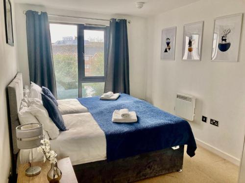 a bedroom with a bed with a blue blanket and a window at VIPAbodes at Woking Central in Woking