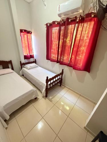 two beds in a room with red curtains at Flat Japaratinga Beach in Japaratinga