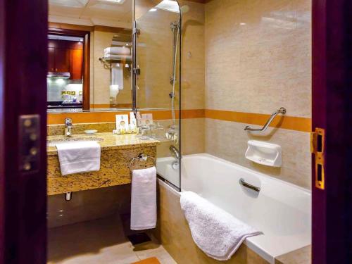 a bathroom with a tub and a sink and a shower at Grand Mercure Majlis Residences Abu Dhabi in Abu Dhabi