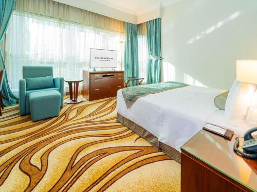 a hotel room with a bed and a chair and a television at Grand Mercure Majlis Residences Abu Dhabi in Abu Dhabi