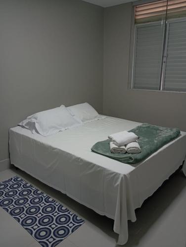 a white bed with a green blanket and a window at Conforto setor Oeste garagem 505 in Goiânia