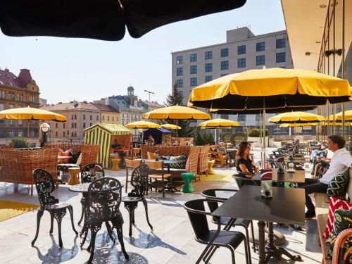 eine Terrasse mit Tischen, Stühlen und gelben Sonnenschirmen in der Unterkunft Mama Shelter Prague in Prag