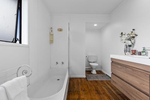 a white bathroom with a tub and a toilet at Beach Haven - Papamoa Beach Escape in Papamoa