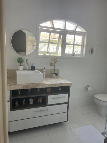 a bathroom with a sink and a mirror and a toilet at Bela casa com piscina in Mongaguá