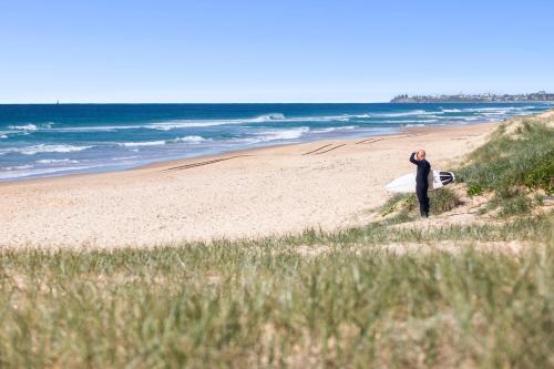 un homme debout sur une plage tenant une planche de surf dans l'établissement Ocean Villa Prime Bokarina Beach Location with Pool, à Bokarina