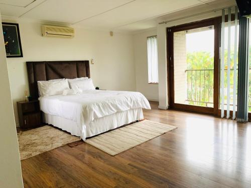 a bedroom with a white bed and a wooden floor at Ezendalo Guest House in Pinetown