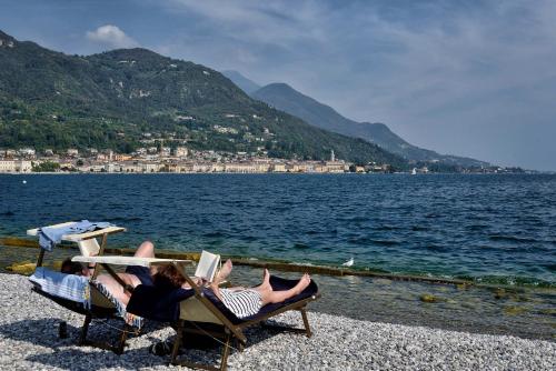 two people laying in chairs on a beach with a book at Antico Teatro signorile in Salò