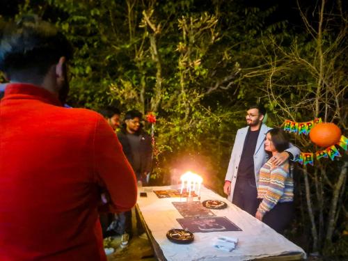 een groep mensen die rond een tafel staan met een verjaardagstaart bij The Rawscape hostel in Kausani