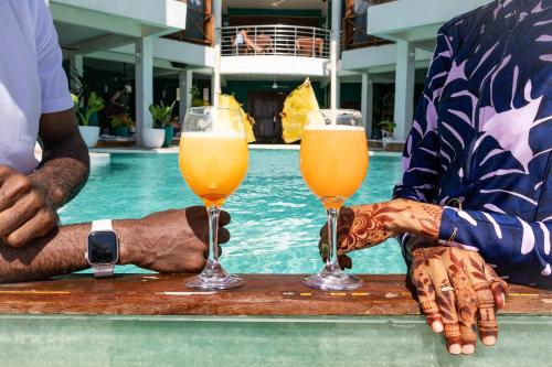 due persone che tengono in mano dei drink su un tavolo vicino a una piscina di ZAN Tropical Jambiani Beach a Bwejuu