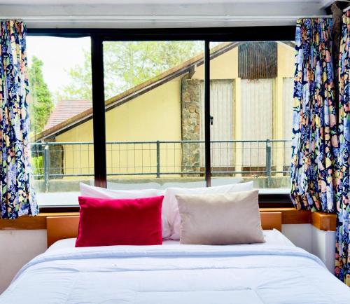 a bed with two red pillows in front of a window at 5BR Villa with Private Pool Lembang in Bandung