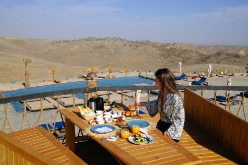 a woman standing at a table with food on a deck at SEVEN SAINTS Lodges in El Karia