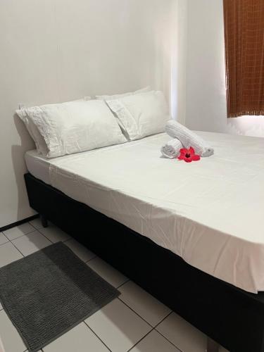 a bed with white sheets and a red flower on it at 1 Quarto passos da praia in Fortaleza