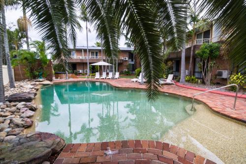 una piscina con una palma accanto a un edificio di The Galaxy Motel a Gosford