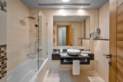 un bagno con vasca, lavandino e specchio di Copthorne Hotel Sharjah a Sharjah