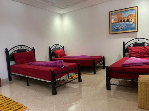 three beds with red pillows in a room at Taghazout surf in Tamraght Ouzdar