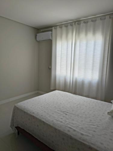 a white bedroom with a bed and a window at Casa Jardim dourado in Porto Belo