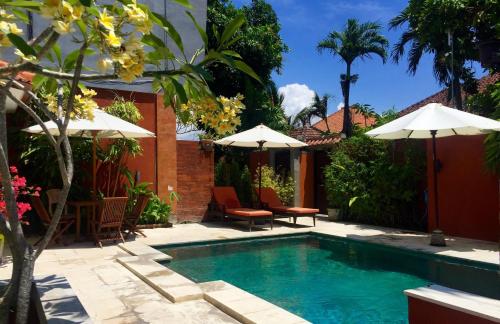 a swimming pool with umbrellas and chairs next to a house at Merpati - Studios in Sanur