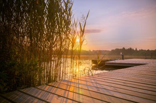 a dock with the sun setting over a body of water at Dabintos slėnis in Sumiliszki