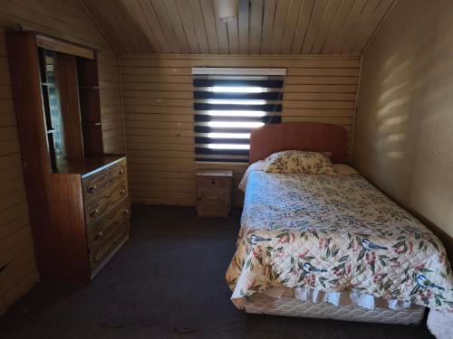een slaapkamer met een bed, een ladekast en een raam bij Lago Chelenko in Chile Chico