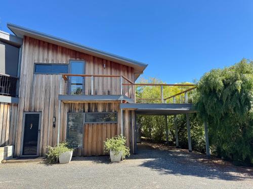 a wooden house with a balcony and a tree at Saje's House & Pod in Myrtleford