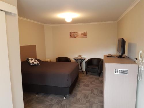 um quarto com uma cama, uma televisão e cadeiras em Mandurah Foreshore Motel em Mandurah