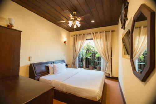 een slaapkamer met een bed, een plafondventilator en een raam bij Bualuang Hotel in Luang Prabang
