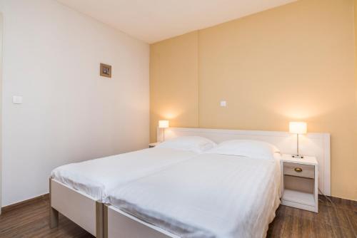 a bedroom with a large white bed and two lamps at Apartments Amfora Plava Laguna in Umag