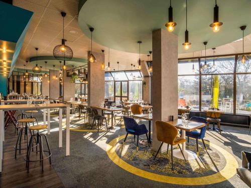 een restaurant met tafels, stoelen en ramen bij Novotel Le Mans in Le Mans