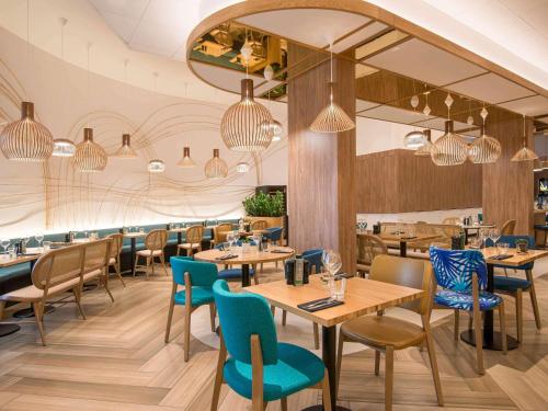 a restaurant with wooden tables and blue chairs at Novotel Nice Arenas Aeroport in Nice