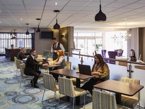 un gruppo di persone seduti ai tavoli con computer portatili di Novotel Coventry a Coventry