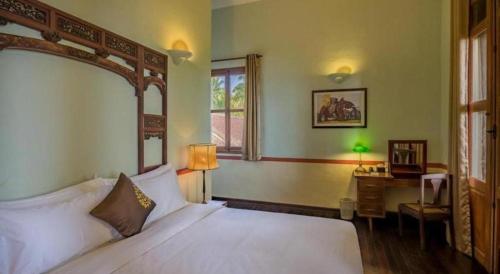 a bedroom with a white bed and a desk and a window at Le Relais de Chhlong in Chhlong