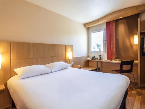 een slaapkamer met een groot wit bed en een bureau bij Ibis Château-Thierry in Essômes-sur-Marne