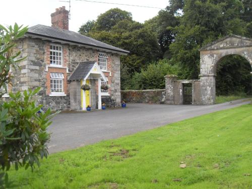 an old stone house with a yellow door and a driveway at Cloverhill Gate Lodge in Cloverhill