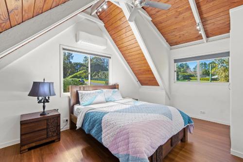 a attic bedroom with a bed and two windows at Mountain Escape Cozy 3-Bedroom Retreat with Outdoor Entertaining in North Tamborine