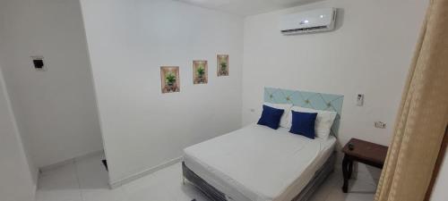 ein weißes Schlafzimmer mit einem Bett mit blauen Kissen in der Unterkunft Hostal y Piscina in La Romana