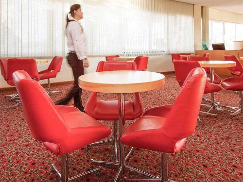 una donna in piedi in una stanza con sedie e tavoli rossi di ibis Uberlandia a Uberlândia
