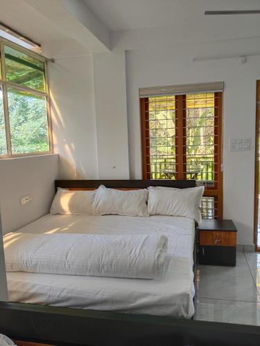 a bedroom with a bed with white sheets and windows at V Land Homestay in Vagamon