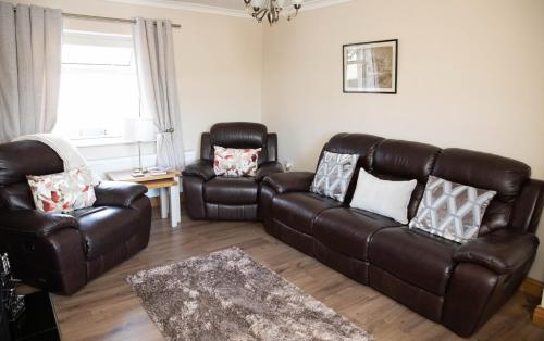 a living room with a leather couch and two chairs at Katies Cottage in Gortaclare