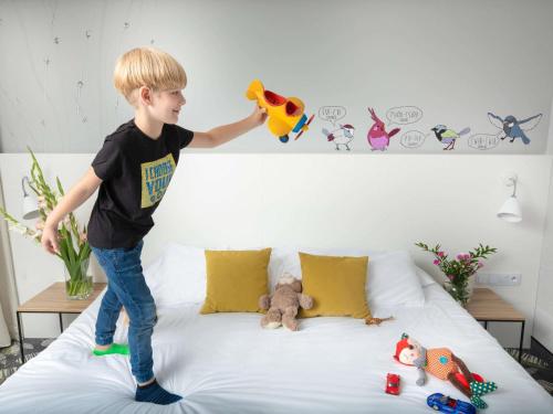 a young boy standing on a bed playing with toys at ibis Styles Bialystok in Białystok