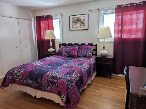 1 Schlafzimmer mit einem Bett mit einer lila Decke und 2 Fenstern in der Unterkunft Bungalow in Green Area in Ottawa