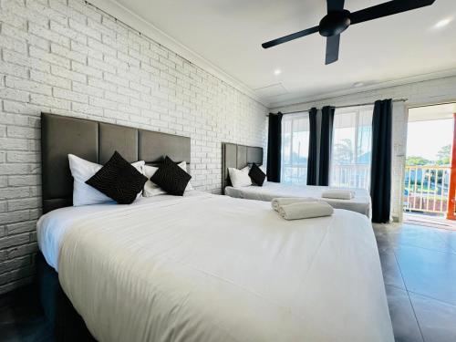 two white beds in a bedroom with a brick wall at Aussie Rest Motel in Cessnock