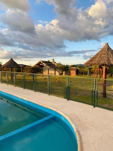 a fence with a swimming pool in front of a field at Complejo de cabañas El Nido in Mina Clavero
